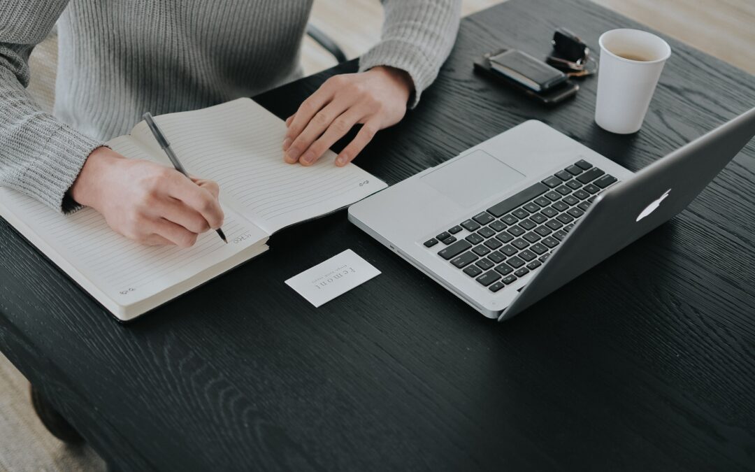 Hands taking notes with a computer open doing research on a raise from their employer